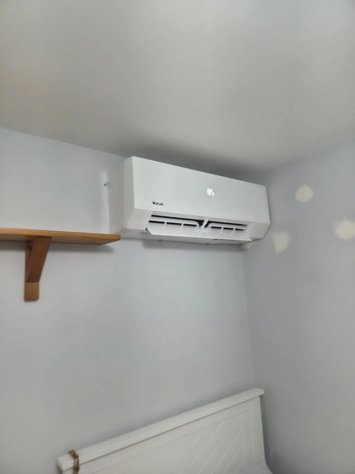 Ductless wall unit in a small bedroom beside a shelf