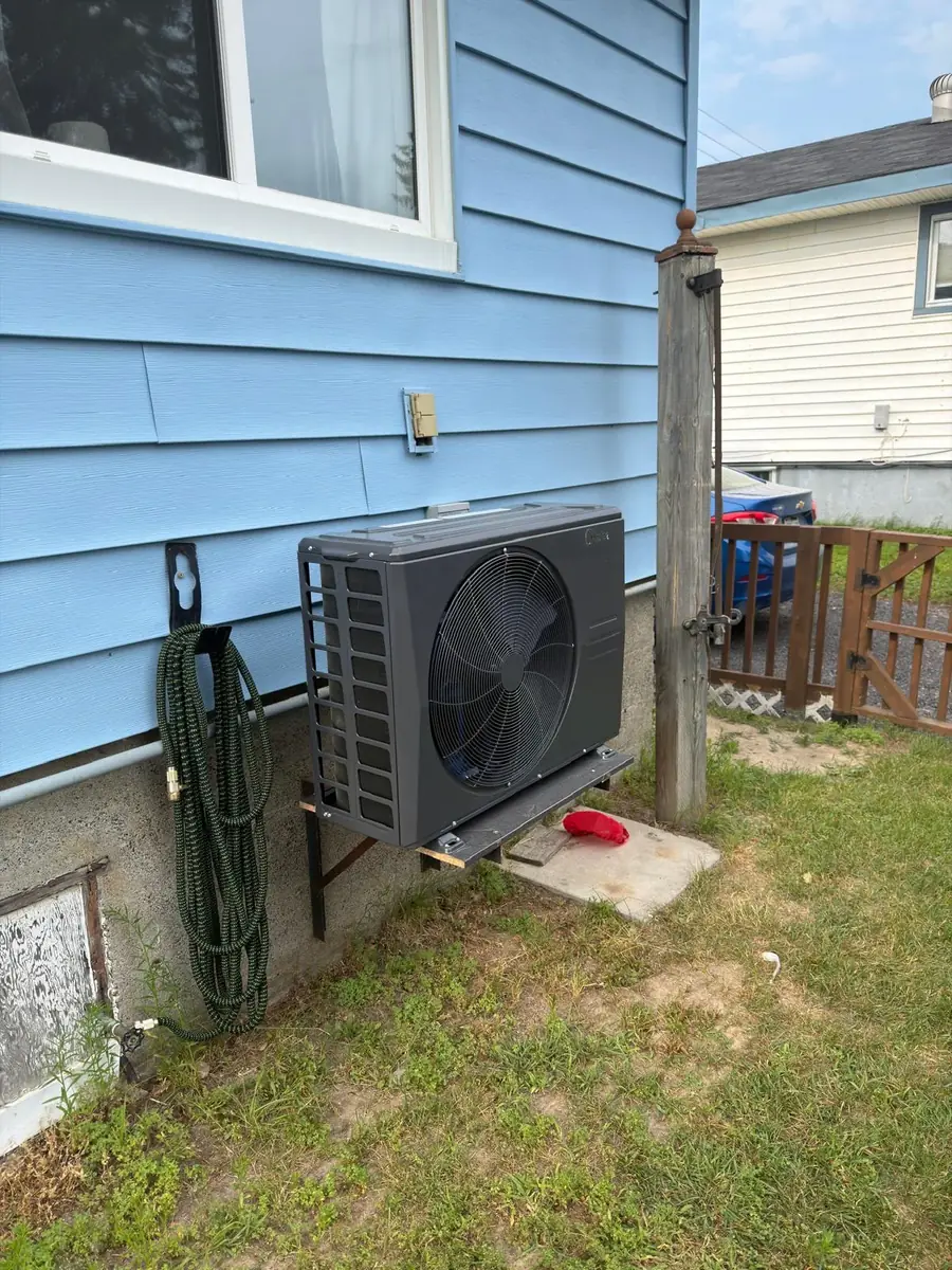 Midea cold-climate heat pump on a wall bracket beside blue siding