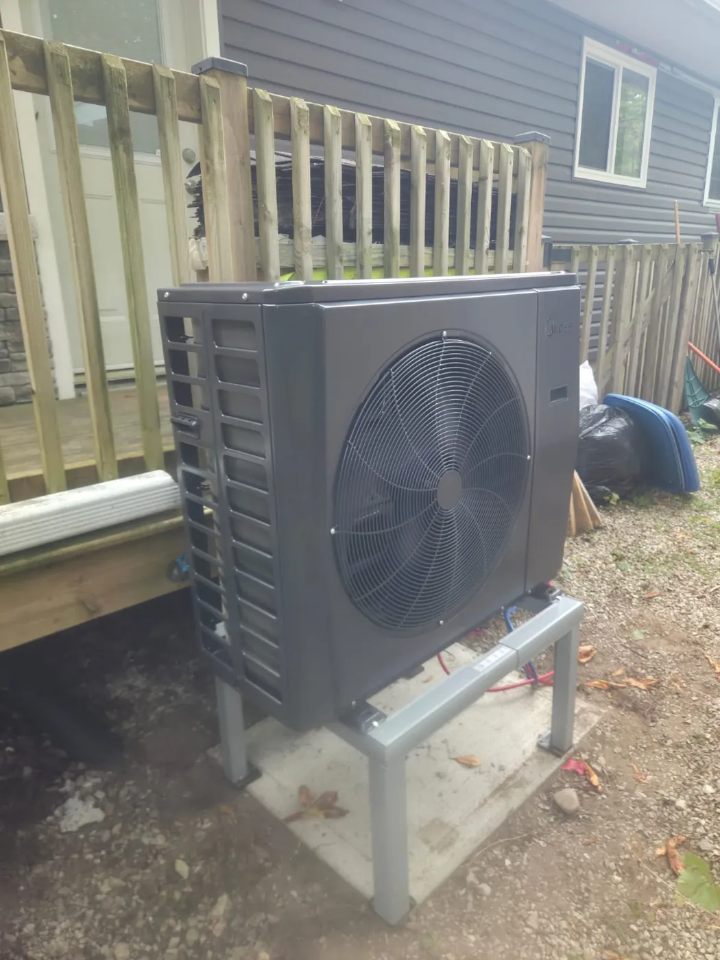 Midea cold-climate heat pump on a stand beside a deck fence, installed by EHI