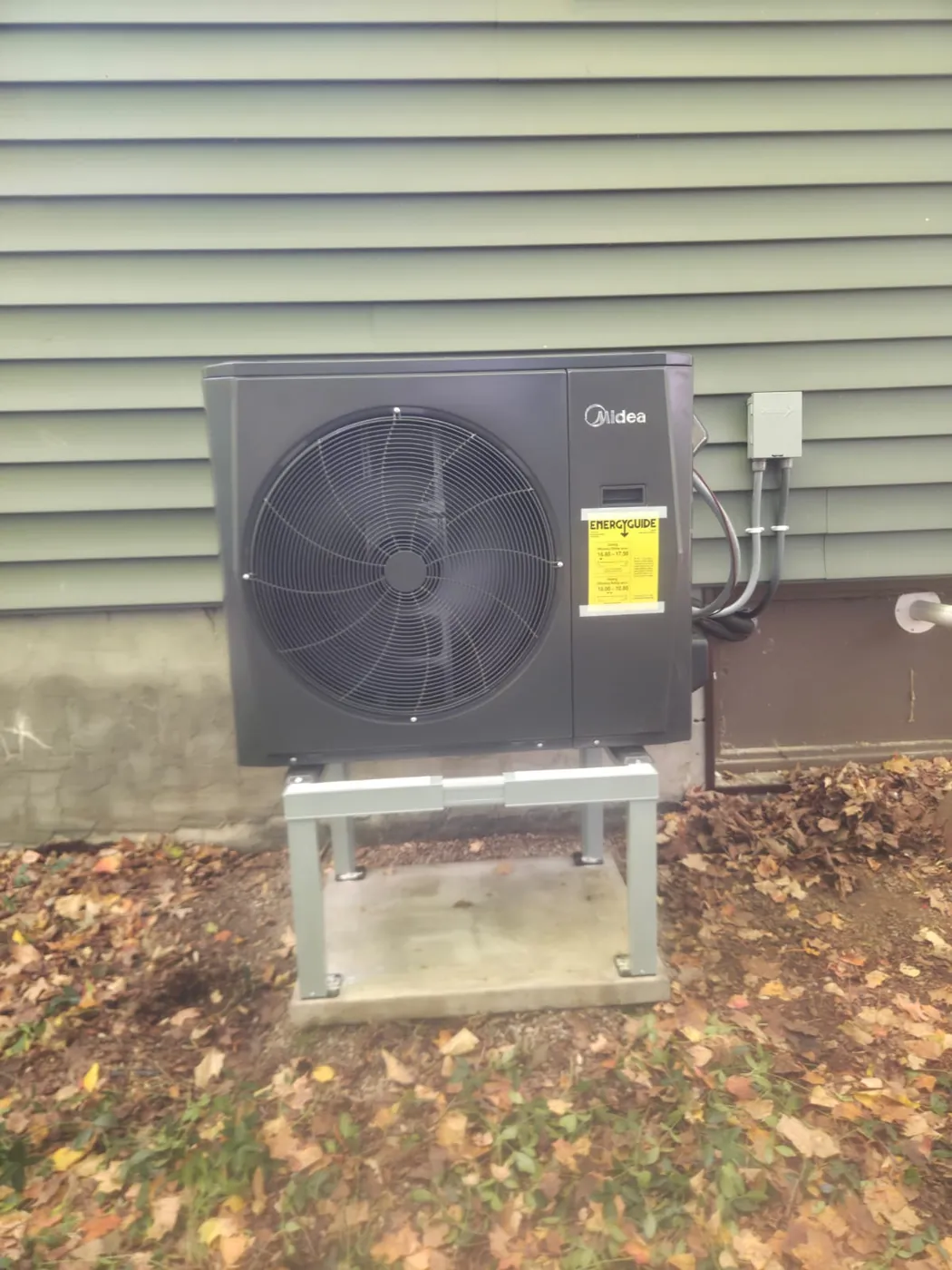 Midea cold-climate heat pump on a raised stand with outdoor disconnect, installed by EHI