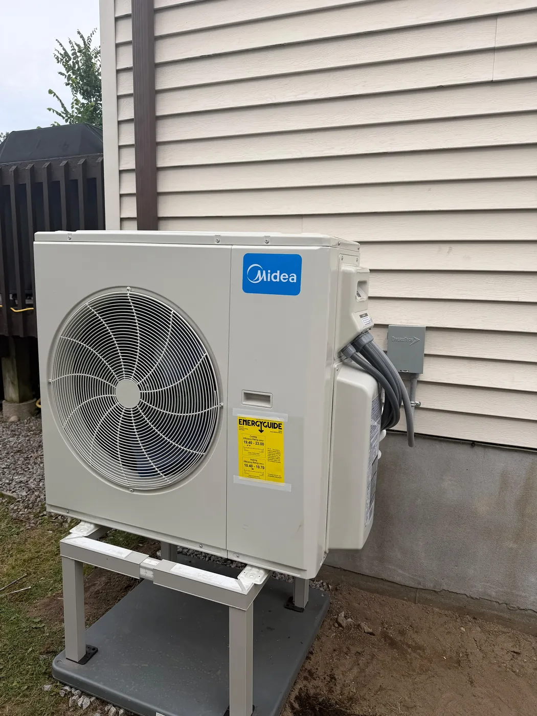 Midea outdoor unit on a stand beside vinyl siding, installed by EHI