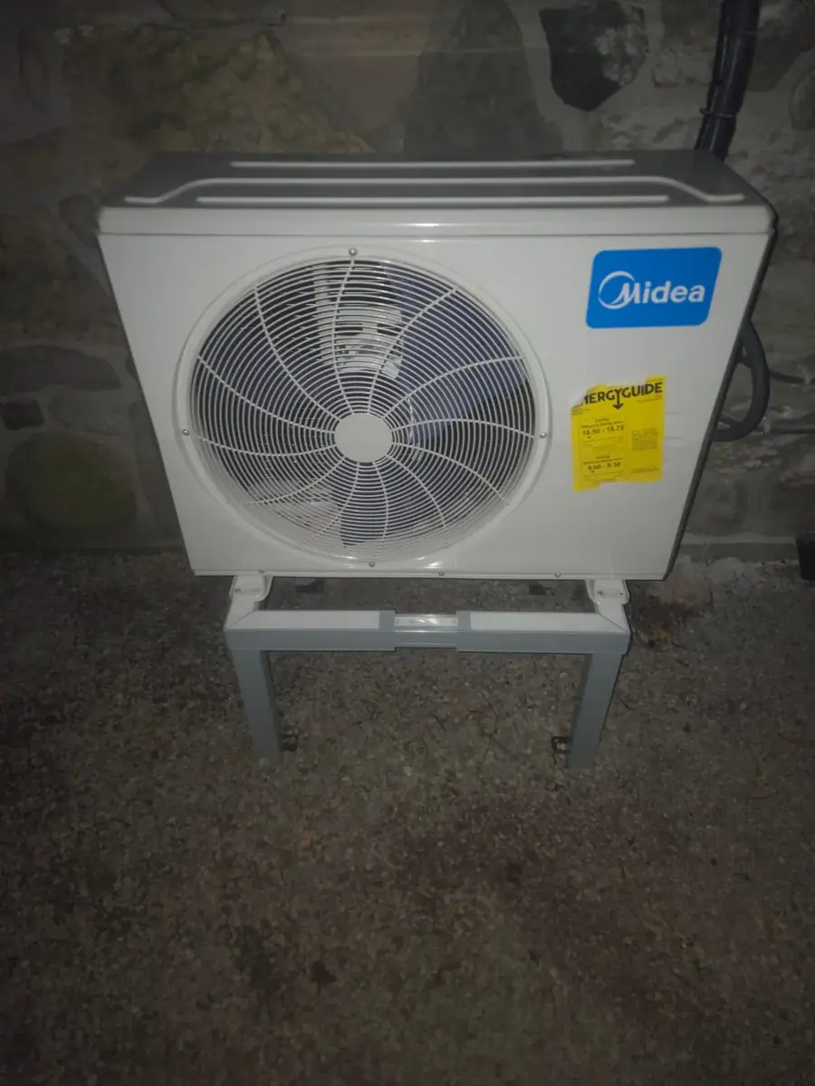 Midea outdoor unit on a stand beside a stone foundation