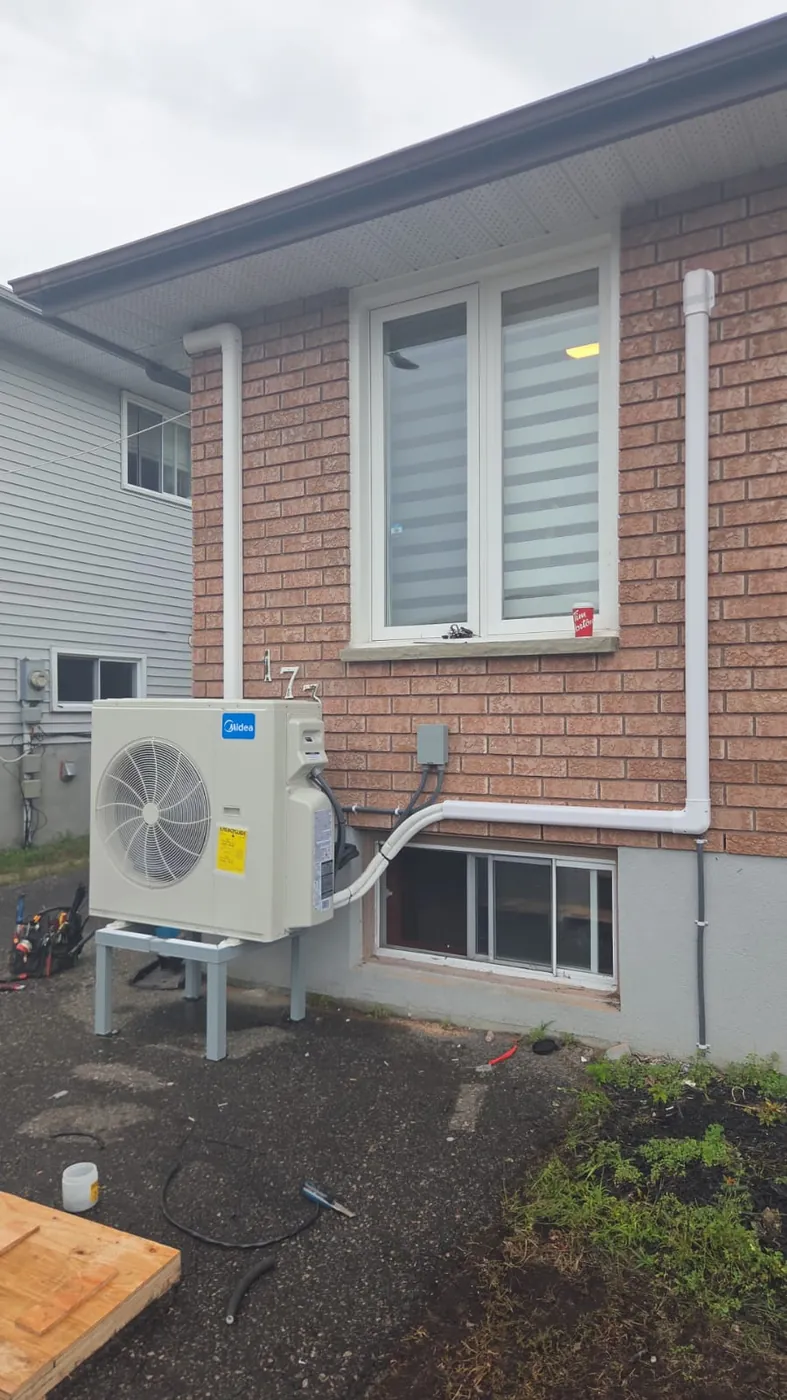 Midea outdoor unit beside a brick bungalow with line set cover up the wall