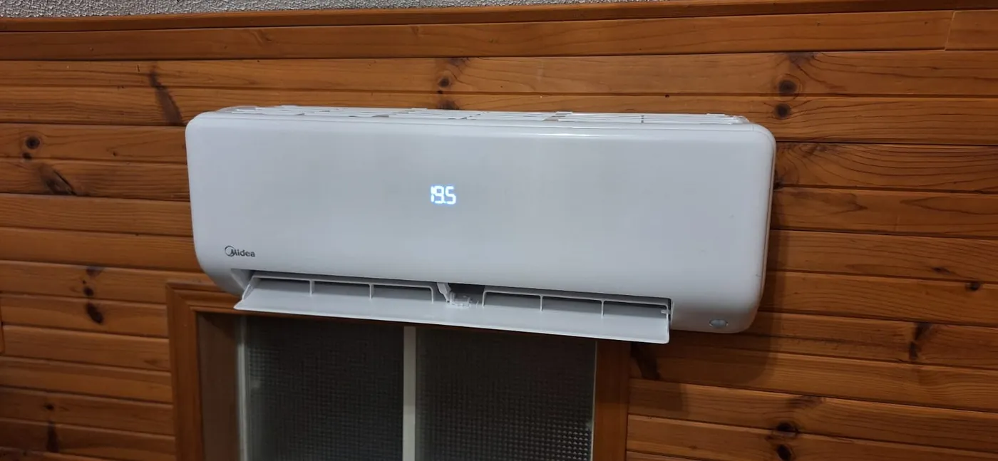 Midea ductless head above a window on a pine-panelled wall